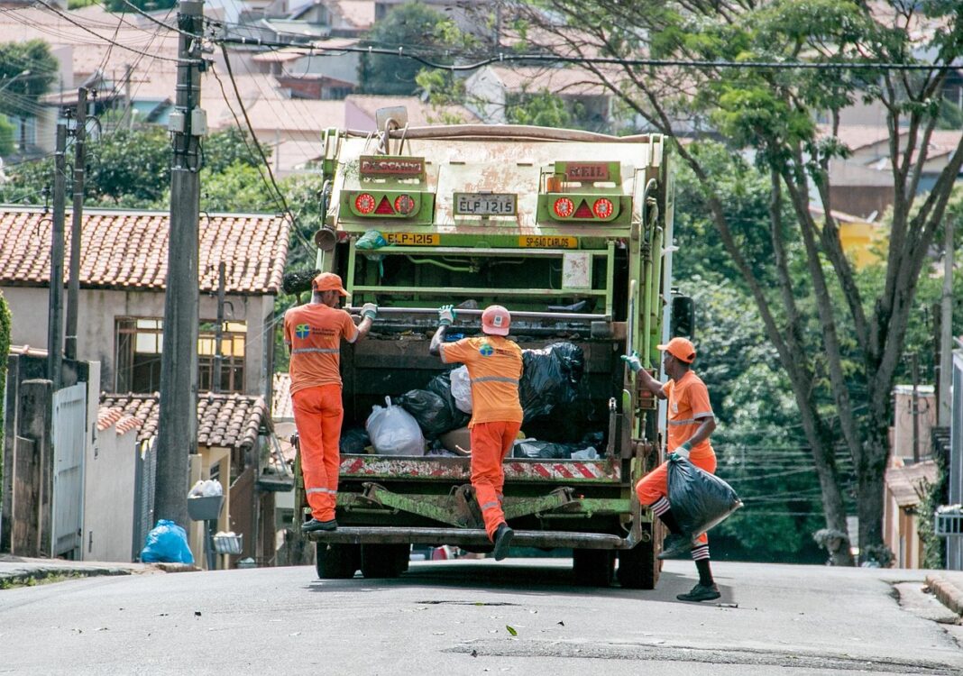 O masina de gunoi transporta trei persoane care strang deșeurile